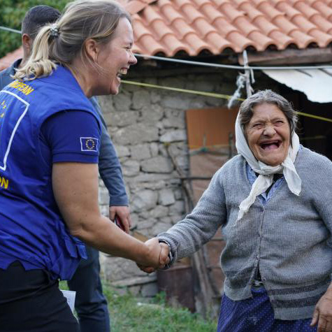 Aid worker and old woman shaking hands while laughing.