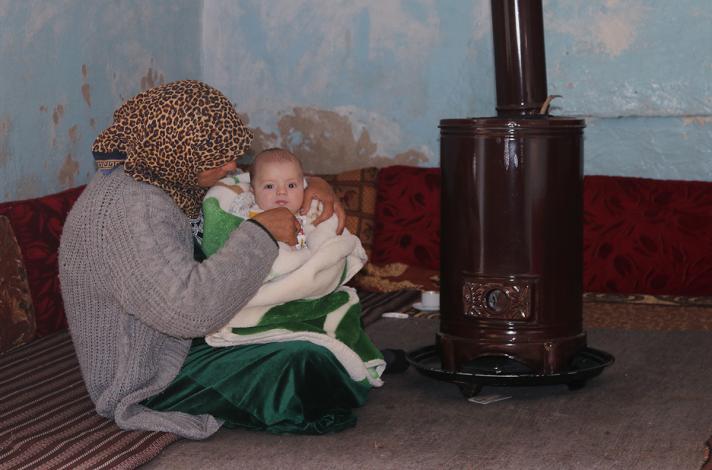 Woman with child sitting on the ground, in front of a stove
