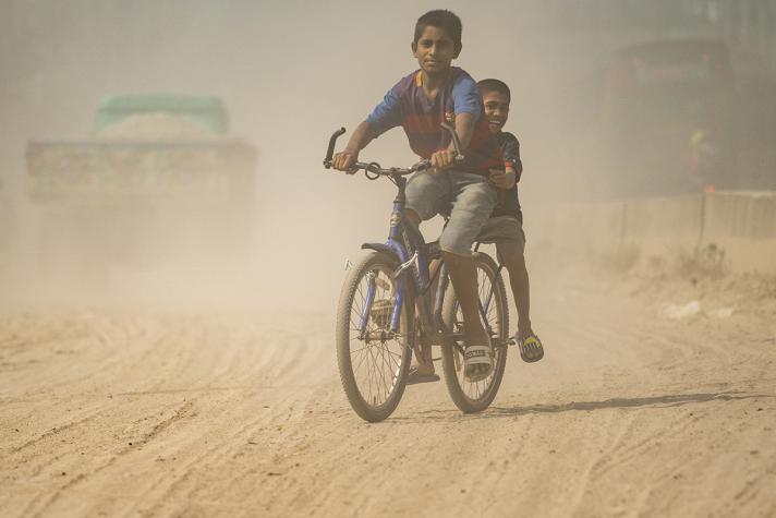 2 children riding a bike in a dusty atmosphere