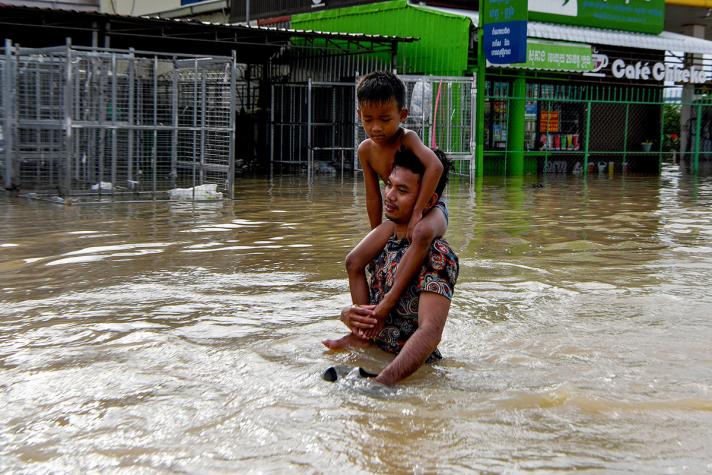 A father with his child on his shoulders, standing in a flooded street