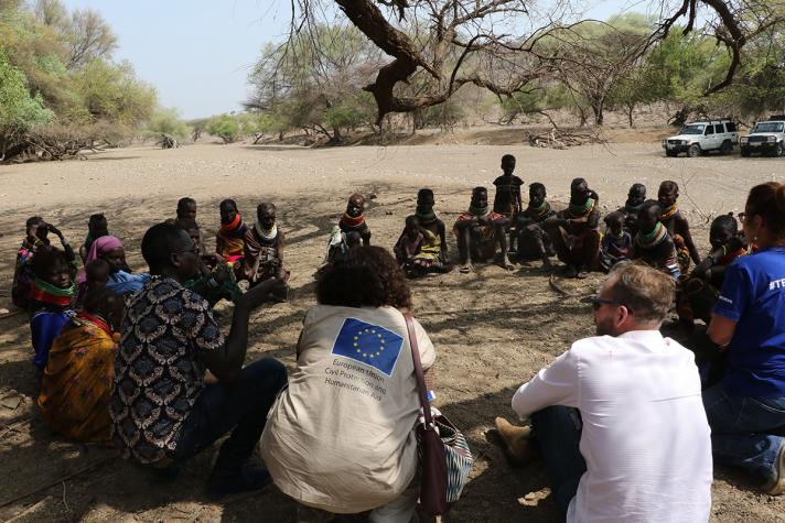 Villagers with aid workers sitting in a circle under a tree