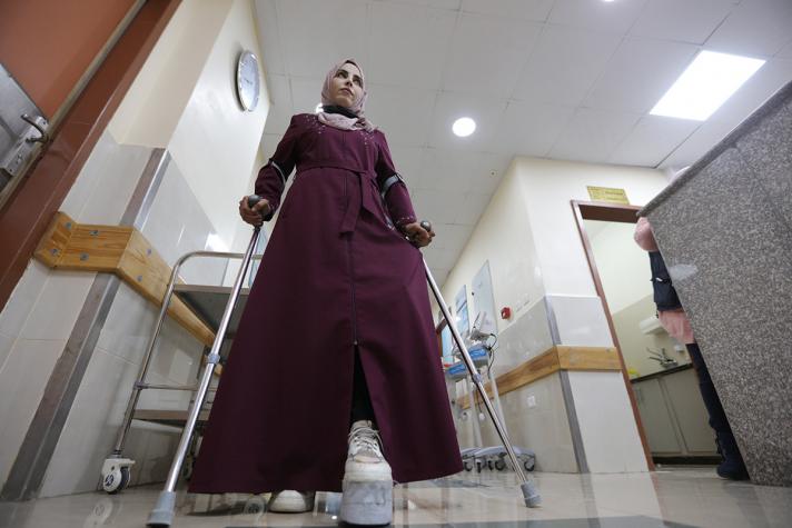 Mayada wearing her custom made shoe while walking with crutches in the hospital hall way