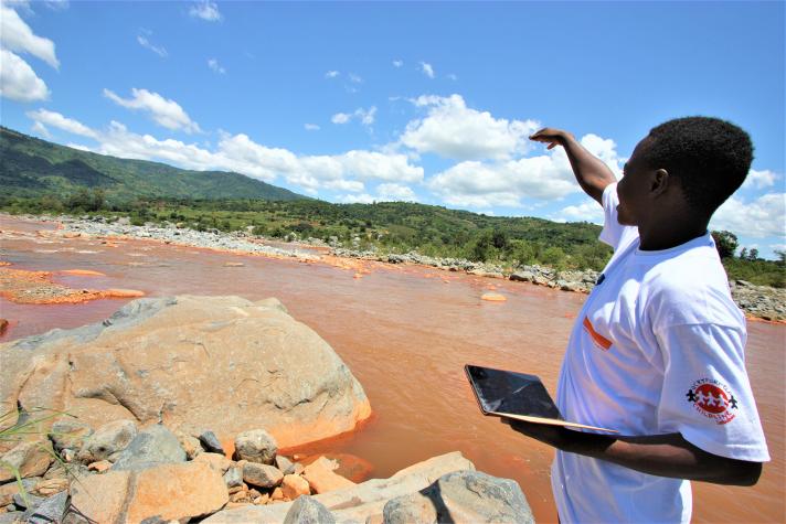 A student holding up a tablet while pointing towards a flooded field