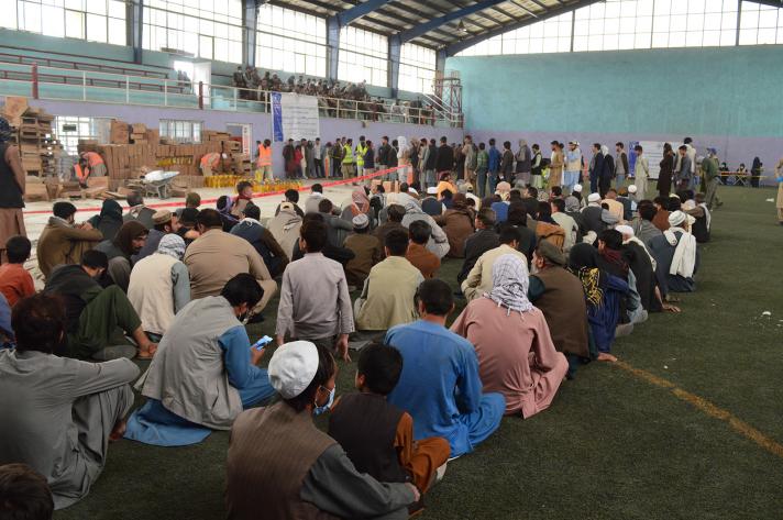 People sitting on the ground in a great hall waiting for food distribution