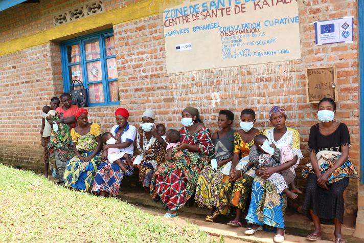 Mothers sitting in a row on a bench outside at the Katala health center