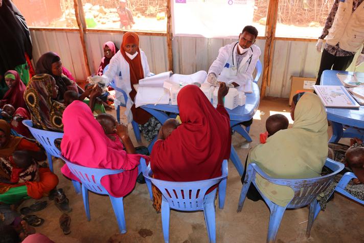 Mothers, sitting in a circle on chairs, are shown how to treat malnutrition