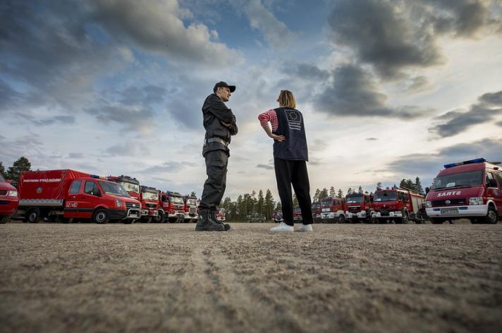 2 people standing on a field surrounded by fire fighting trucks