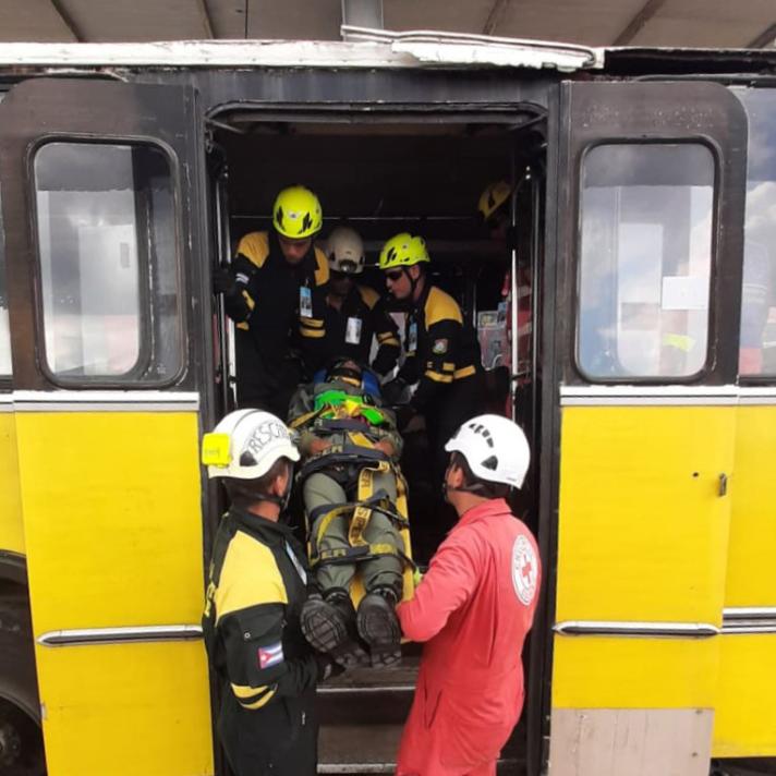 A bus with open doors while aid workers get a person on a stretcher out of it.