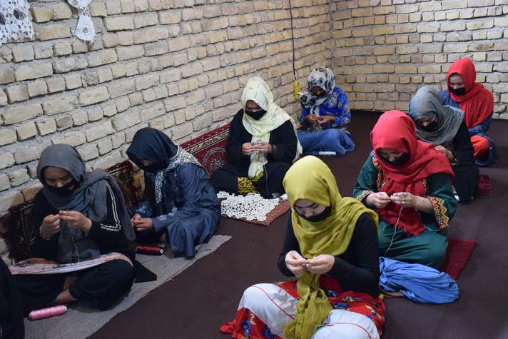 Women sitting on the ground in 2 rows while embroidering.