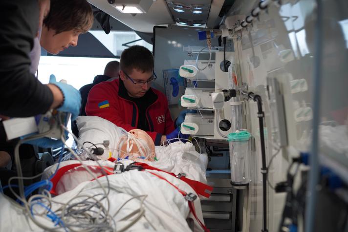 Person being helped, lying in an ambulance, by 3 doctors.