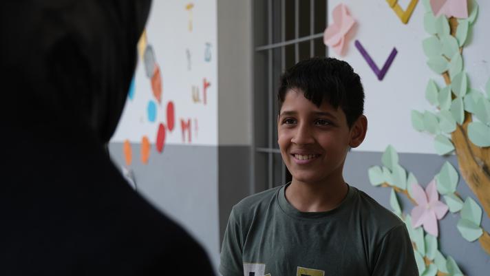 Mostafa speaking to another person. In the back, part of the school outdoor wall.