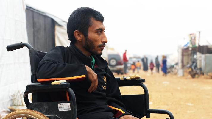 Close up of person sitting in a wheelchair, in the background a view of the shelter settlement