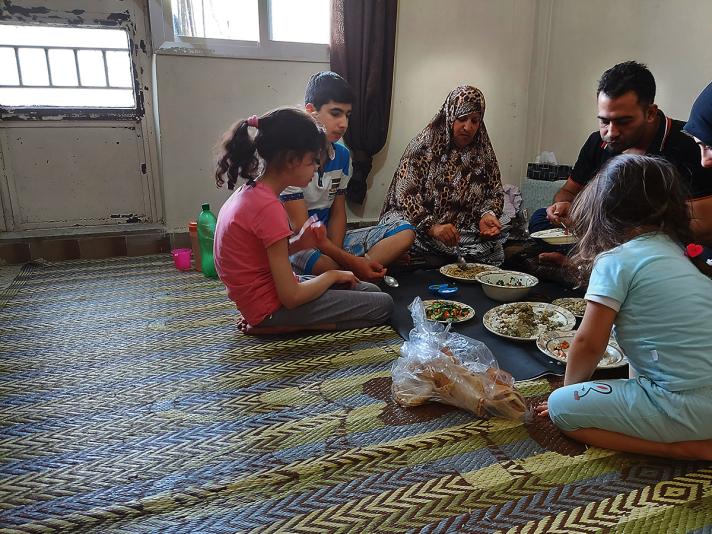Yasmeen and her family sharing a meal, sitting on the floor while all kind of dishes are inbetween them.