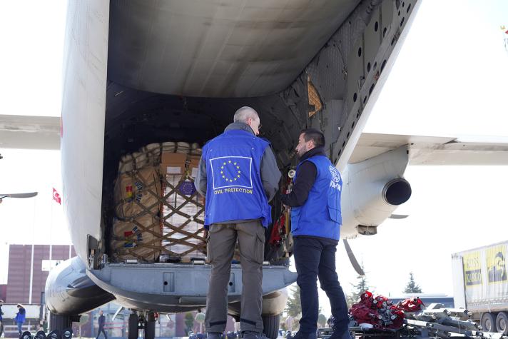 2 aid workers in front of a plane while unloading stockpiles.