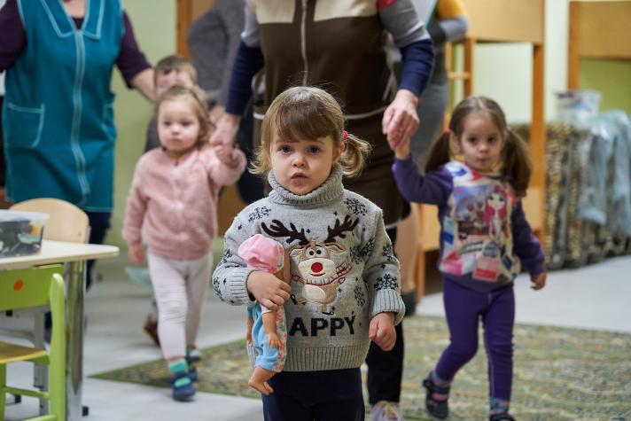 3 children standing in a kindergarten each holding a plush toy
