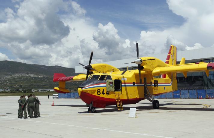 Small group of people in front of a bright yellow firefighting plane.