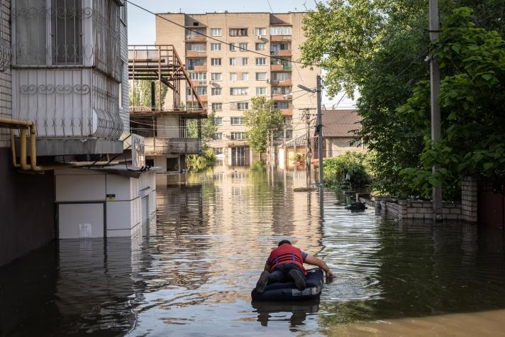 Man in a rubber boat amidst a flooded street.