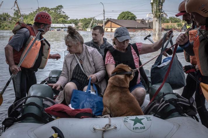 People and a dog being evacuated in a rubber boat.