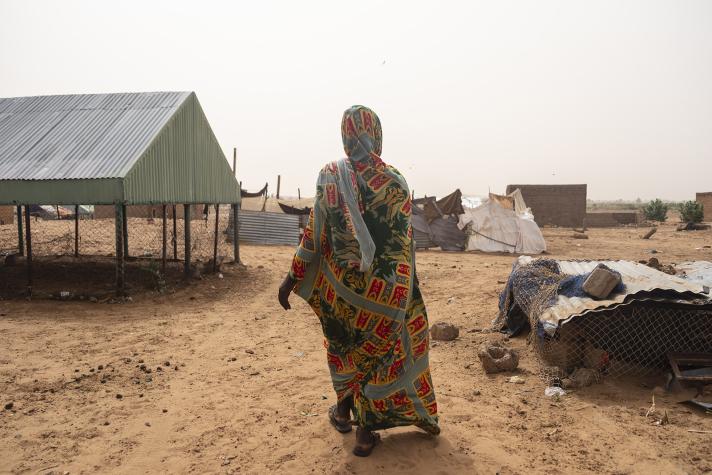 A woman walking inbetween a partially destroyed town.