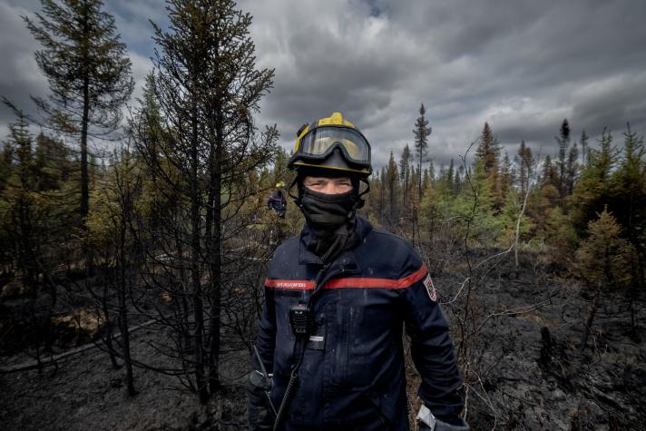 A firefighter, masked for protection from smoke and insects. In the background the woodlands 