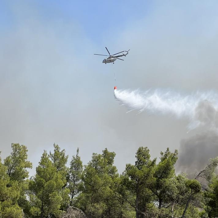 Helicopter dropping air over a fire in a forest.