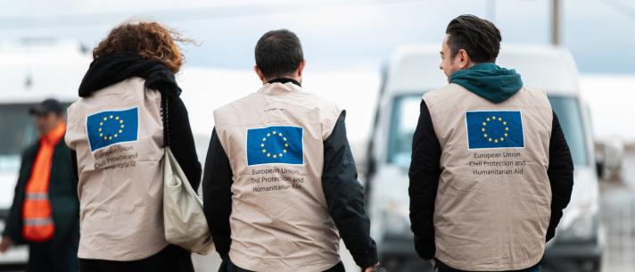3 aid workers seen from the bakc, wearing a jacket with the EU flag on it.