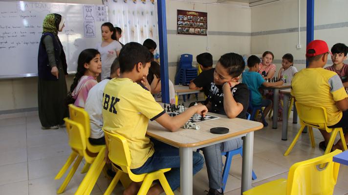 View of a classroom, in front childrens seated at a table playing a game of chess.