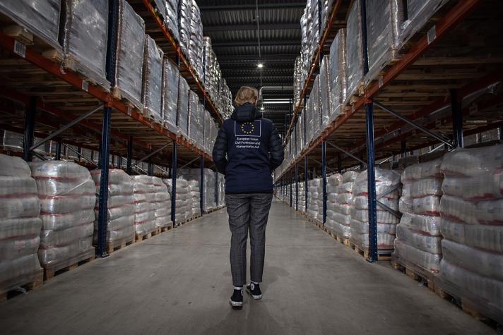 An aid worker amidst 2 high stocks in a warehouse.