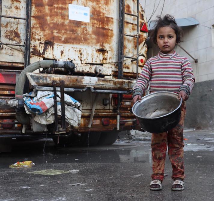 A young girl holding an empty pan walking in a street.