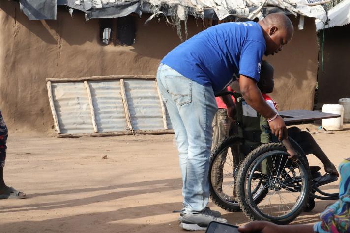 An aid worker helping a boy in a wheelchair on how to make use of it.