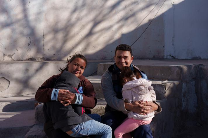 Natalia and José, each holding one of their children, sitting outside on a stairs.