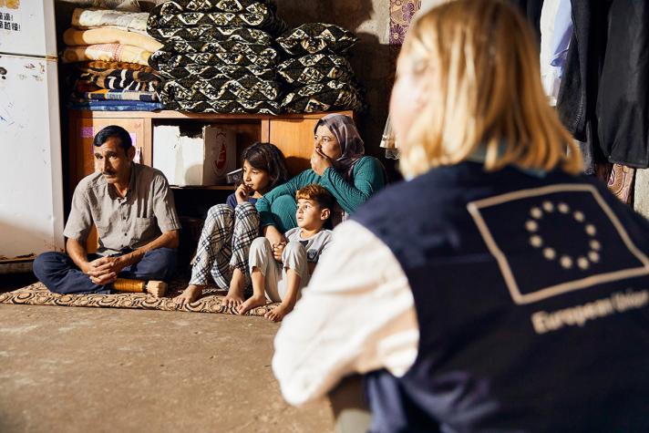 Aid worker talking to Naif and his family while being seated at the floor.