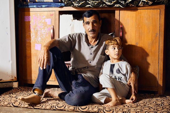Naif and a son sitting in front of a cabinet.