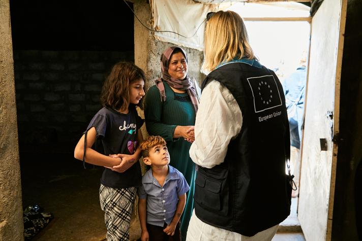 Aid worker talking to the mother and children while standing in a doorway.