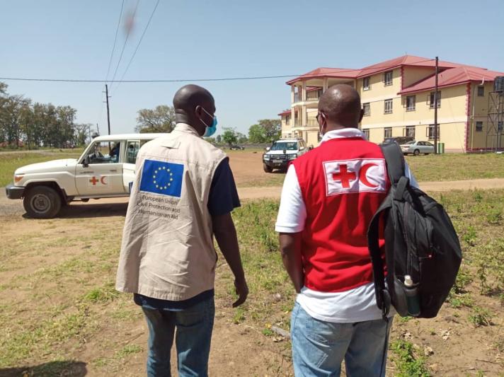 An Ugandan Red Cross aid worker together with an ECHO colleague walking towards a hospital. Several cars are in the back.