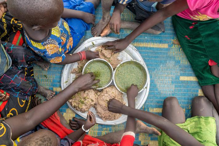 Hands of children and adults taking food from a plate and bowls in the middle.