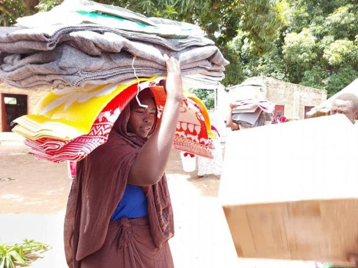 A woman carrying several blankets on her head