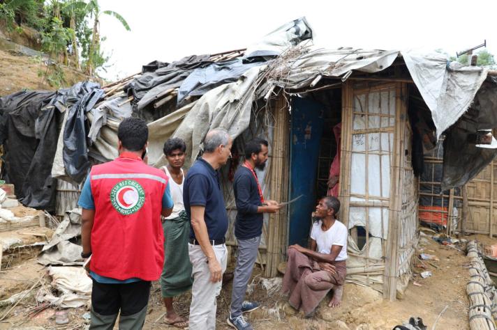 Aid workers talking to a woman who sits outside her house in front of a door.