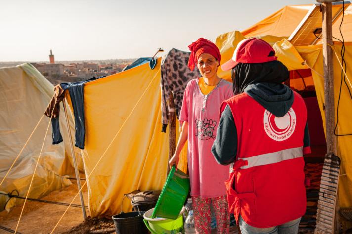 A woman in front of a shelter tent talking to an aid worker.