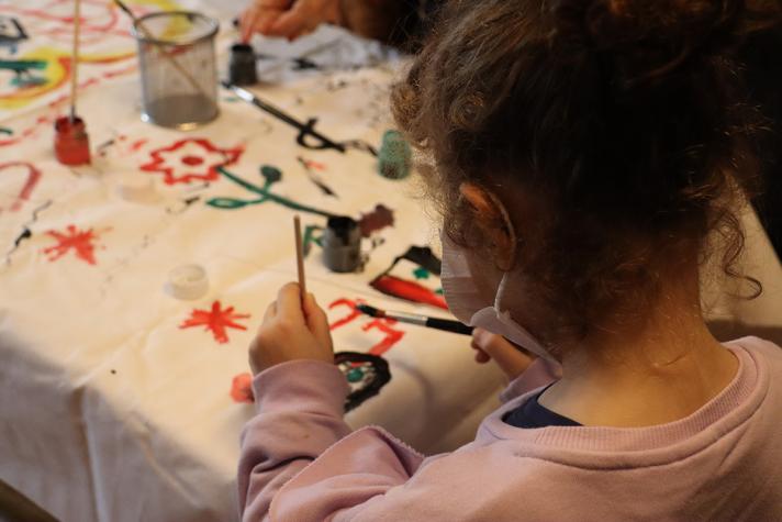 A girl sitting at a table making a painting with flowers and stars.