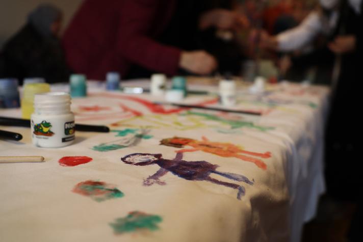 View of the painting and paint jars on the table, in the background a group of women.