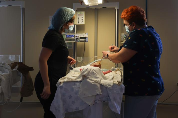2 female health care workers giving aid to a new born in a hospital room.
