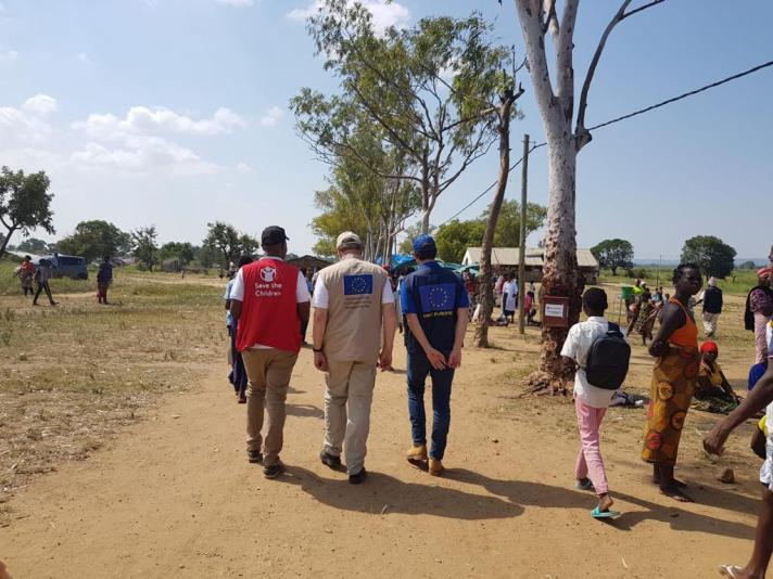 Group of aid workers walking on a road towards a small village.