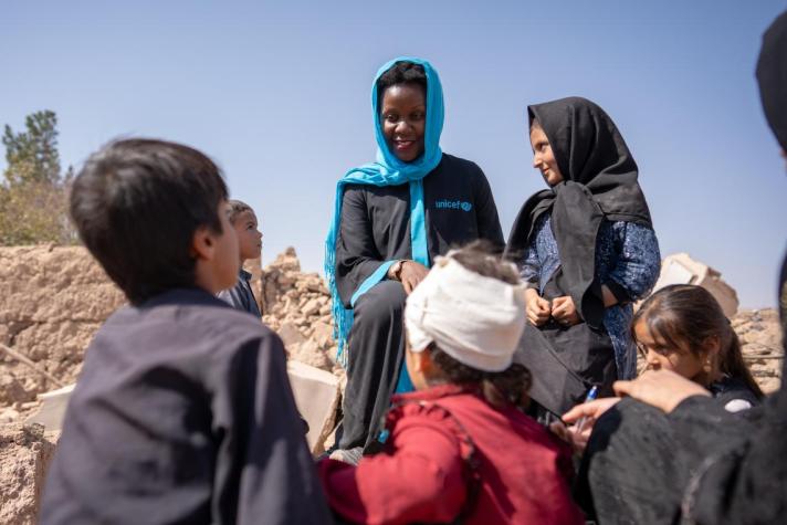 Group of children, seen from the back, talking to a Unicef aid worker.