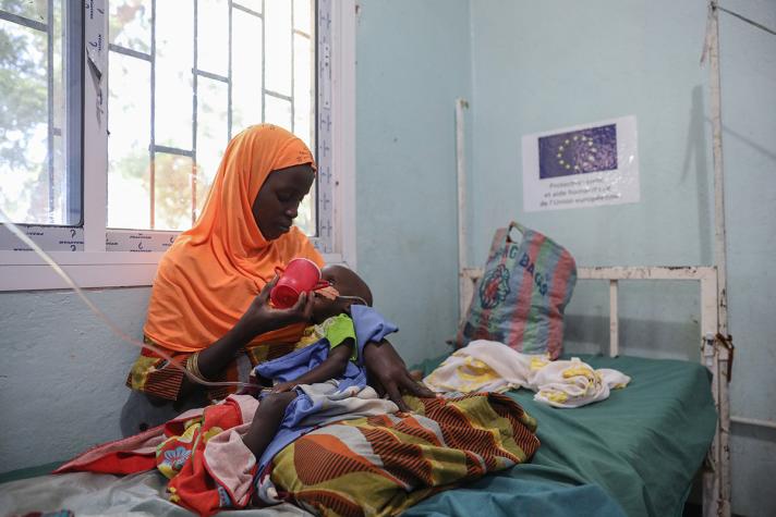 Djibri feeding her child while sat on a bed in the health centre.