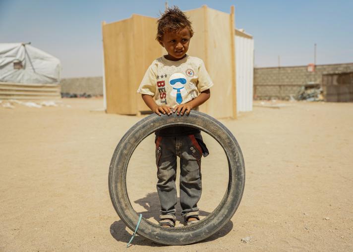 A boy holding a tire - as a toy - in the background a structure and walls.