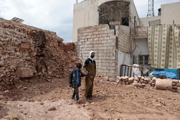 A man and a young boy standing in front of a partly collapsed building.