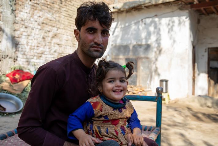 Naseer with his daughter Zakia outside sitting on a chair.