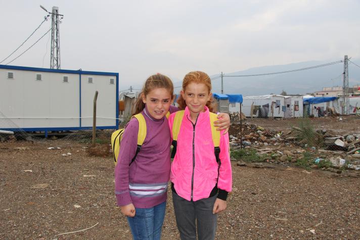Aysa and Eslem holding each other while standing in front of a container school.