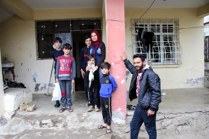 Mohamed, Zari and 5 children of different age stand in front of their partly damaged house.